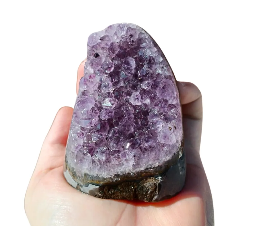 An amethyst cluster with a cut base, held in the hand